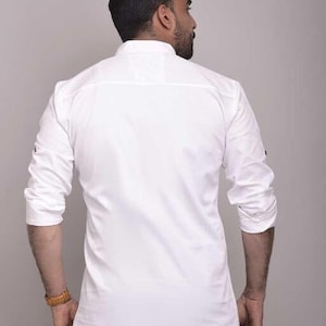 Pu&ograve; includere: Camicia bianca a maniche lunghe con colletto alla coreana. La camicia ha polsini con bottoni e un orlo curvo. La vista posteriore mostra il design e la vestibilit&agrave; della camicia. La camicia &egrave; di colore bianco.