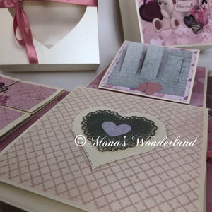 Op de afbeelding: Een verzameling handgemaakte papieren ambachten, waaronder een hartvormige doos met een lint en verschillende versierde dozen met hart- en bloemmotieven. Het kleurenschema is voornamelijk roze en cr&egrave;me, met decoratieve elementen.