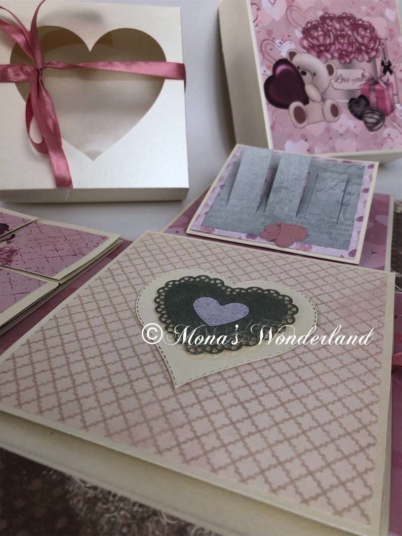 Op de afbeelding: Een verzameling handgemaakte papieren ambachten, waaronder een hartvormige doos met een lint en verschillende versierde dozen met hart- en bloemmotieven. Het kleurenschema is voornamelijk roze en cr&egrave;me, met decoratieve elementen.