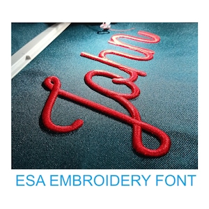 Könnte beinhalten: Nahaufnahme einer roten Stickerei auf einem dunkelblauen Stoff. Das Wort "John" ist in einer kursiven Schrift gestickt.