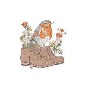 Op de afbeelding: Een geborduurd ontwerp met een roodborstje dat op een paar bruine laarzen zit. De vogel heeft oranje, witte en grijze veren. Bloemen en bladeren omringen de laarzen, alles tegen een witte achtergrond.