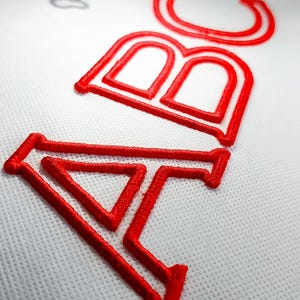 May include: Close-up of red embroidered letters "ABC" on a white fabric.
