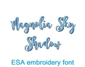 Può includere: L'immagine mostra le parole "Magnolia Sky Shadow" in un carattere ricamato corsivo blu chiaro. Sotto, il testo recita "ESA embroidery font". Il carattere è di stile decorativo.