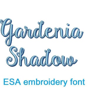 May include: A digital image features the words "Gardenia Shadow" in a cursive, light blue font. Below the words, the text "ESA embroidery font" is displayed in a darker blue color, indicating the font's name and purpose.