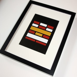 May include: A framed abstract art print featuring a geometric design. The artwork has a black background with rectangular shapes in red, white, and yellow. The print is set within a white mat and a black frame.
