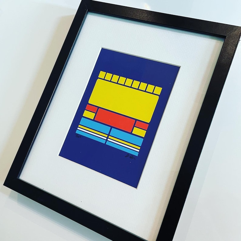 May include: A framed abstract art print with a blue background and geometric shapes in yellow, red, and blue. The print is signed "D.B."