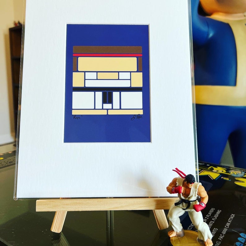 Pode incluir: Uma impress&atilde;o emoldurada de um desenho abstrato geom&eacute;trico em tons de azul, amarelo, branco, vermelho e marrom. A impress&atilde;o est&aacute; em um fundo azul e &eacute; assinada "Ryu" e "Akira".