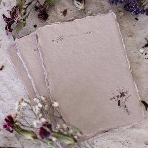 May include: Three sheets of light pink paper with deckled edges. The top sheet has the word "notes" written in cursive and the word "date" written below it. The bottom sheet has a small floral design in brown.