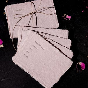 Op de afbeelding: Een stapel roze papieren afspraakkaarten, gebonden met een bruin touwtje. De kaarten hebben de tekst "Appointment" erop gedrukt met de koppen "Occasion", "Date", "Time" en "Details".