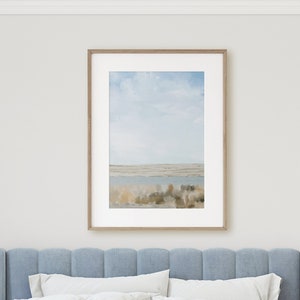 May include: A light blue upholstered bed with a white quilted duvet and two white pillows. The bed is in a bedroom with a framed landscape photograph on the wall and two gold side tables with lamps.