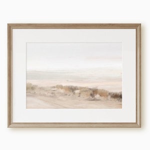 Puede incluir: Una fotografía enmarcada de una escena de playa con una paleta de colores suaves y apagados. La imagen presenta una playa de arena con algunos arbustos pequeños y un cielo brumoso en el fondo.