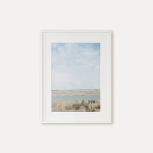 May include: A framed painting of a landscape with a blue sky, white clouds, and a body of water in the distance. The foreground is a field of brown and green grasses.