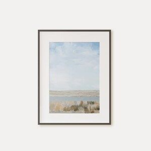 May include: A framed watercolor painting of a landscape with a blue sky, white clouds, and a body of water in the foreground. The water is surrounded by brown and green brush.