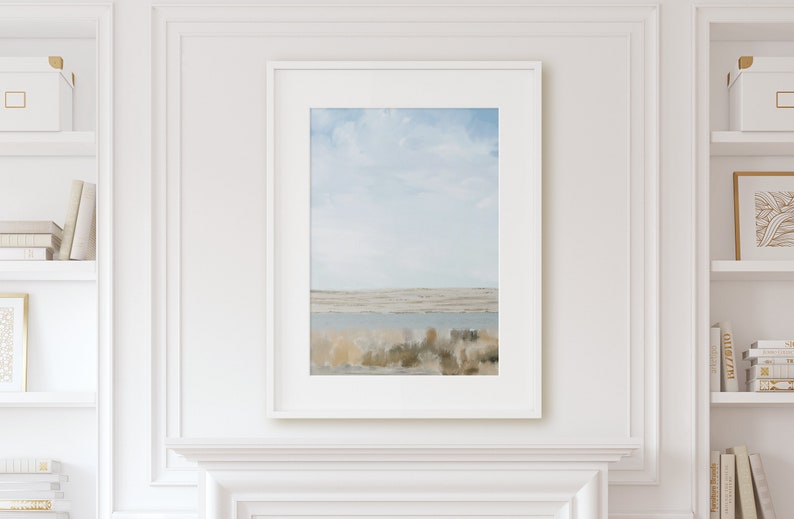 May include: A framed print of a landscape painting with a blue sky, white clouds, and a body of water in the distance. The foreground features a field of brown and green grasses.