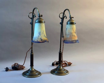 May include: A pair of antique brass table lamps with a decorative floral design. Each lamp has a  swivel arm and a  pale blue and yellow glass shade.