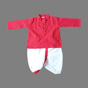 Puede incluir: Un conjunto de kurta y dhoti a rayas rojas y blancas para un beb&eacute; o un ni&ntilde;o peque&ntilde;o. La kurta tiene un cierre de bot&oacute;n y el dhoti es blanco con un ribete rojo.