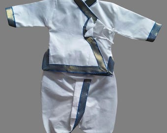 May include: White baby outfit with a long-sleeved shirt and matching pants. The shirt has a mandarin collar and is trimmed with gold and blue ribbon. The pants are dhoti style and also trimmed with gold and blue ribbon.