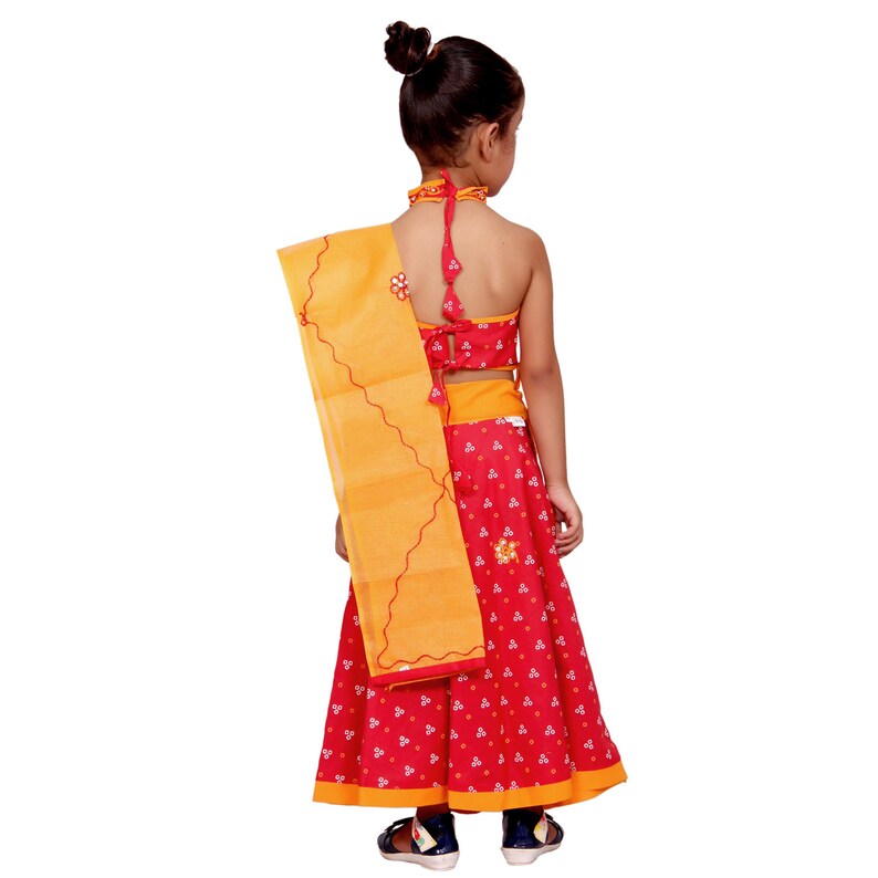 May include: A young girl wearing a red and yellow traditional Indian outfit. The outfit includes a sleeveless top, a skirt with a floral print, and a yellow dupatta.