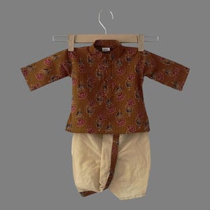 May include: A brown and beige two-piece outfit for a child. The top has a floral print and a mandarin collar. The bottom is a dhoti pant.