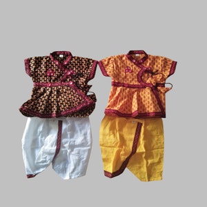 May include: Two children's outfits, one with a black and gold top and white pants, the other with a yellow and gold top and yellow pants. Both outfits have a red trim and a button closure.