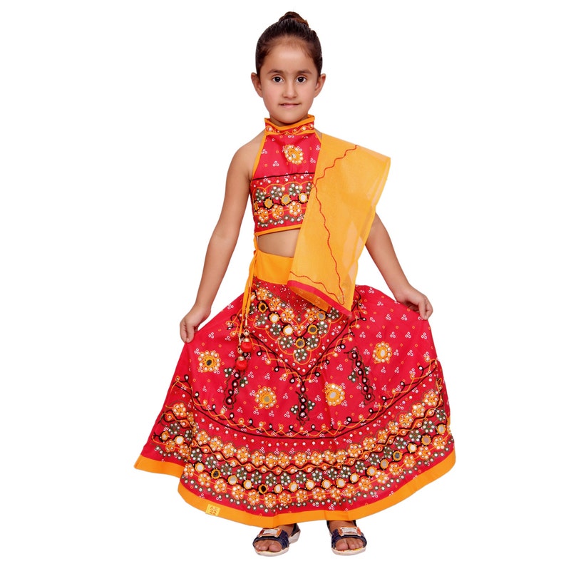 May include: A young girl wearing a red and yellow traditional Indian outfit with a colorful embroidered skirt and a matching top. The skirt is decorated with mirrors and beads.