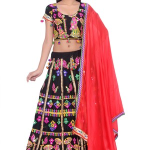 Puede incluir: Una falda negra y colorida bordada con una blusa a juego y un dupatta rojo. La falda tiene un dise&ntilde;o en capas con trabajo de espejo y borlas. La blusa tiene un escote redondo y mangas cortas. El dupatta es una tela transparente con un borde.