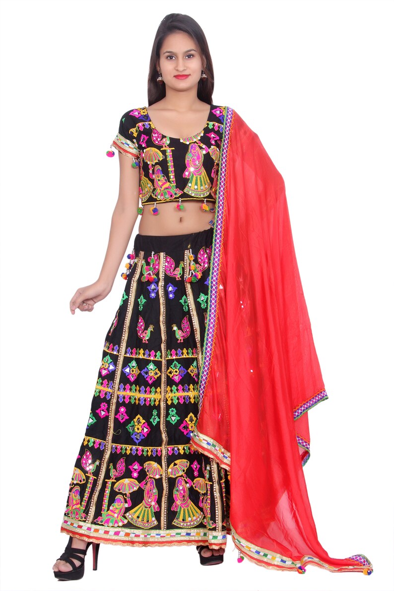 Puede incluir: Una falda negra y colorida bordada con una blusa a juego y un dupatta rojo. La falda tiene un dise&ntilde;o en capas con trabajo de espejo y borlas. La blusa tiene un escote redondo y mangas cortas. El dupatta es una tela transparente con un borde.