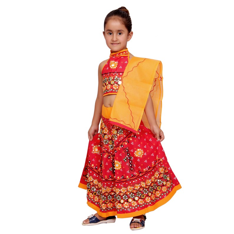 May include: A young girl wearing a red and yellow traditional Indian outfit with a floral print and mirror embellishments. The outfit includes a sleeveless top, a long skirt, and a matching dupatta.