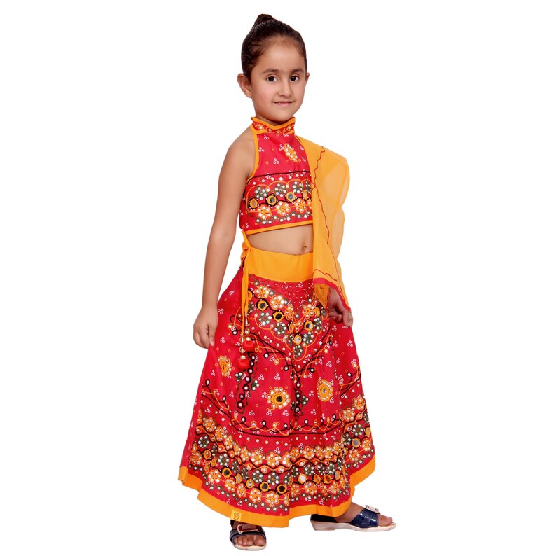 May include: A young girl wearing a red and yellow traditional Indian outfit with a floral pattern and mirror embellishments. The outfit includes a sleeveless choli, a skirt, and a yellow dupatta.