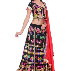 Puede incluir: Una falda negra y colorida bordada con espejos y pompones. La falda se combina con un top corto negro bordado a juego con mangas cortas y pompones. Un dupatta rojo completa el atuendo.
