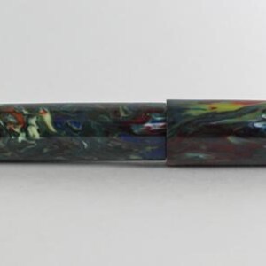 May include: A colorful, marbled fountain pen with a green, blue, red, and white pattern. The pen is closed and lying on a white surface.