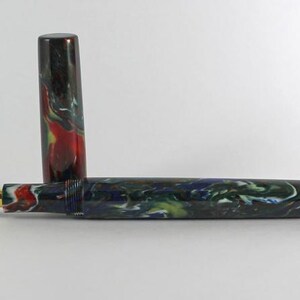 May include: A fountain pen with a black, green, and red marbled body and a gold nib. The pen is closed and the cap is off.