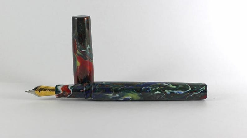 May include: A fountain pen with a black, green, and red marbled body and a gold nib. The pen is closed and the cap is off.