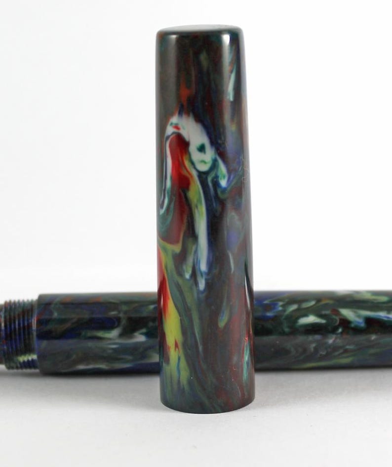 May include: Close-up of a colorful pen cap with a swirling pattern of red, yellow, blue, and white. The pen cap is made of a dark, mottled material.