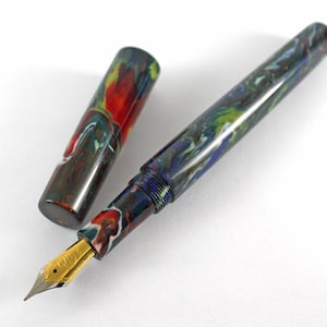 May include: A fountain pen with a colorful, marbled, blue, green, and red resin body and a gold nib. The pen is open and the cap is lying next to it.