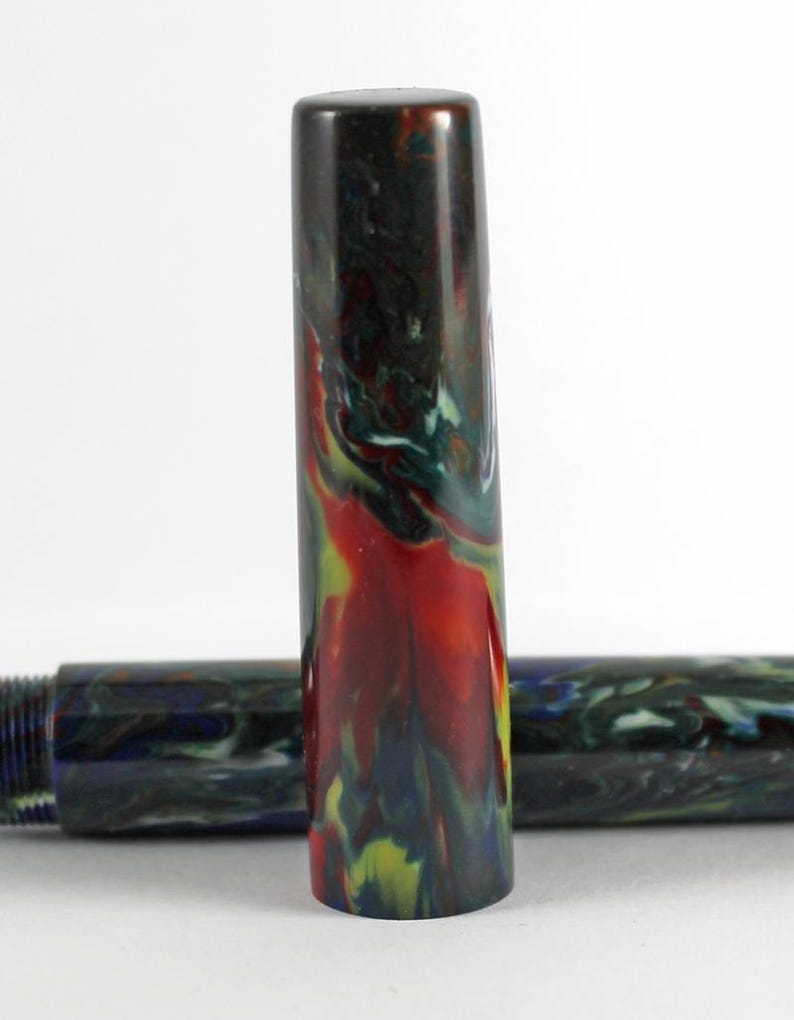 May include: A close-up of a red, green, and blue marbled pen cap. The cap is made of a smooth, glossy material.