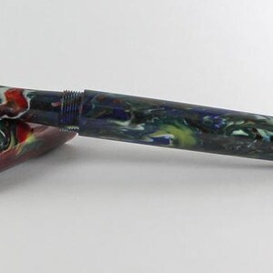 May include: A black and blue fountain pen with a gold nib and a colorful marbled design. The pen is capped and lying on a white surface.