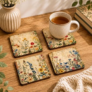 May include: A set of four square coasters featuring a vintage-style botanical print of colorful wildflowers on a cream background. One coaster supports a speckled ceramic mug filled with tea, while the others are arranged nearby.