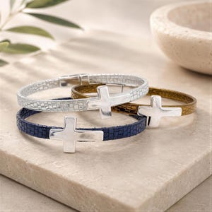 May include: Three bracelets featuring a textured, grid-patterned band in silver, bronze, and navy blue. Each bracelet is adorned with a smooth, polished silver-toned cross charm centered on the band, secured with a metallic clasp closure.