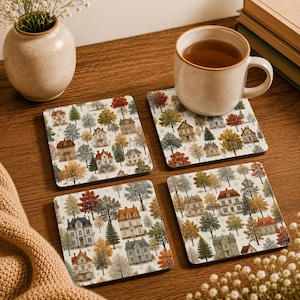 May include: A set of four square coasters featuring a repeating pattern of multi-story houses surrounded by various trees in shades of orange, yellow, green, and grey. The coasters have a white background and are arranged on a wooden surface.