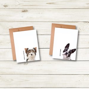 Two greeting cards with images of dogs are placed on a wooden surface.