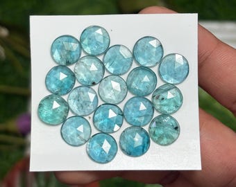 May include: A collection of round, faceted gemstones in shades of blue and teal. The gemstones are arranged on a white card, showcasing their clarity and color. The gems are likely for jewelry making.