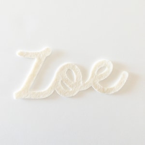 Op de afbeelding: Witte vilt letter uitsnijding van de naam "Zoe" in een cursief schrift.