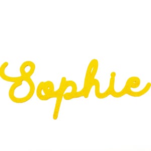 May include: A yellow cursive word "Sophie" against a white backdrop. The word is written in a flowing, handwritten style, with a cheerful and playful design. The colour is a bright, sunny yellow.