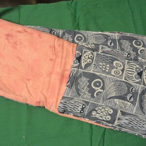 Op de afbeelding: Twee stoffen zakjes, een roze en een blauwe met een wit uilenpatroon. De zakjes zijn gevouwen en liggen op een groene ondergrond.