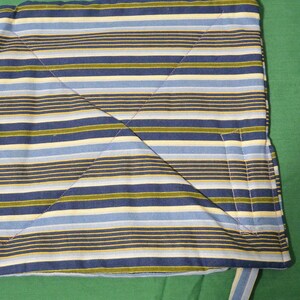 May include: A striped fabric cushion with blue, yellow, and green stripes. The cushion is folded in half and has a seam down the center.