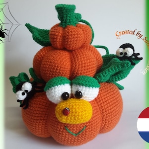 Puede incluir: Una pila de calabazas de crochet con una cara amigable, dos arañas negras y hojas verdes. La calabaza de abajo es la más grande, con las calabazas más pequeñas apiladas encima. Las calabazas son de color naranja y las hojas son verdes. Las arañas tienen cuerpos negros y ojos blancos. El texto "Creado por Sanne Fitzer" es visible en la esquina superior derecha de la imagen.