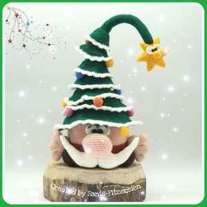 May include: A crocheted Christmas tree gnome with a green hat, a pink face, and a white beard. The gnome is wearing a red and white striped scarf and is holding a yellow star.