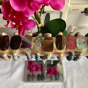 May include: Eight agate stone bracelets with gold accents and grey lava beads. Each bracelet features a different color and pattern of agate.