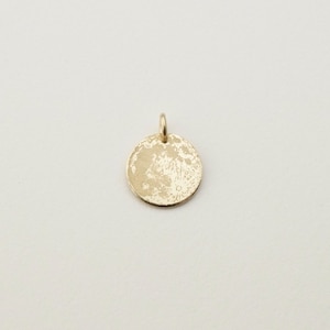 May include: A circular gold pendant featuring a detailed, textured relief of the moon's surface on its front face. The pendant includes a small, integrated jump ring at the top for attachment to a chain, showcasing a metallic finish.